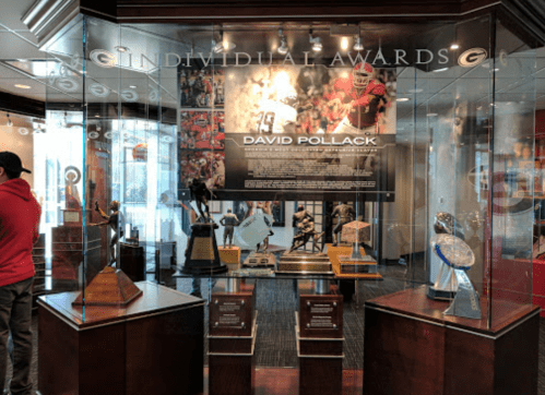 Display case featuring individual awards, including trophies and a plaque for David Pollack, in a sports museum setting.