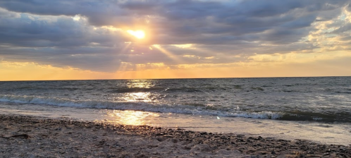 A serene beach scene at sunset, with golden rays shining through clouds over gentle waves and sandy shore.