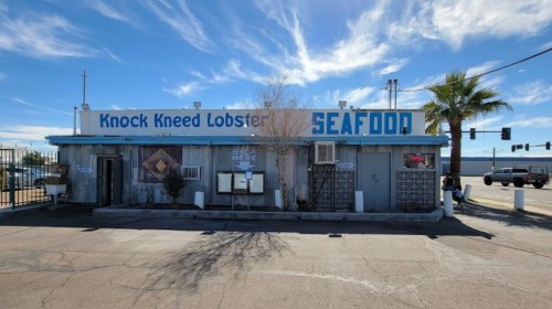 A seafood restaurant named "Knock Kneed Lobster" with a blue sign, palm tree, and clear sky in the background.