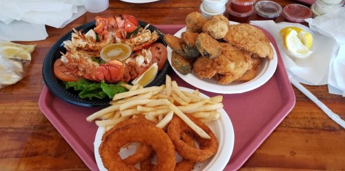 A tray with fried seafood, including lobster, fried fish, onion rings, and French fries, garnished with lemon and sauces.