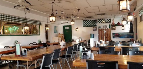 A cozy restaurant interior with wooden tables, black chairs, and vintage lanterns hanging from the ceiling.