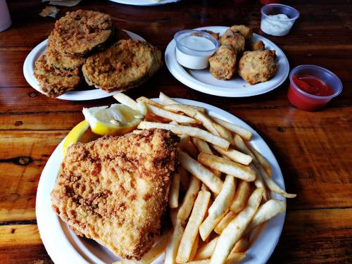 A plate of fried fish with fries and lemon, accompanied by two smaller plates of fried food and dipping sauces.