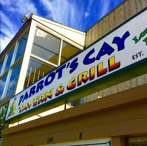 Sign for Parrot's Cay Tavern & Grill, featuring colorful lettering against a blue sky backdrop.