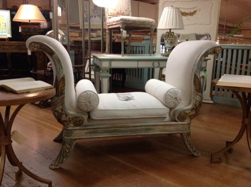 A vintage-style white upholstered chair with ornate wooden details and curved arms, set in a cozy interior space.