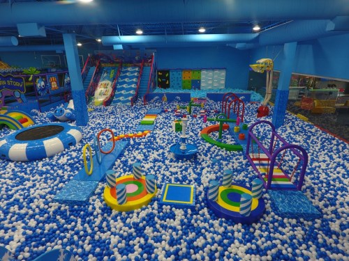 A colorful indoor play area filled with blue and white balls, featuring slides, climbing structures, and various play equipment.