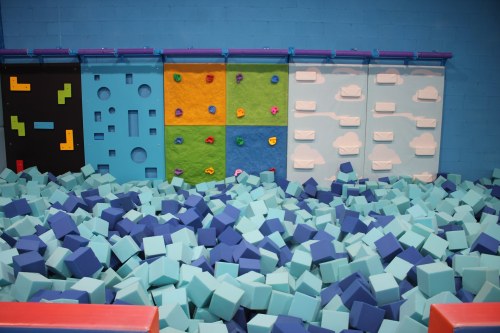 A colorful foam pit with climbing walls in a play area, featuring blue and green foam blocks scattered throughout.