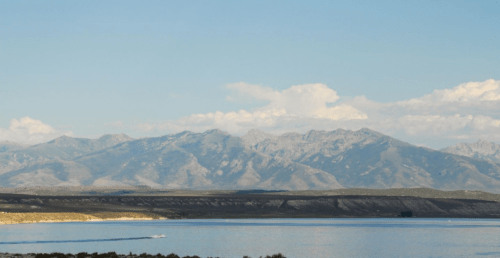 A serene landscape featuring mountains in the background and a calm lake in the foreground under a clear blue sky.