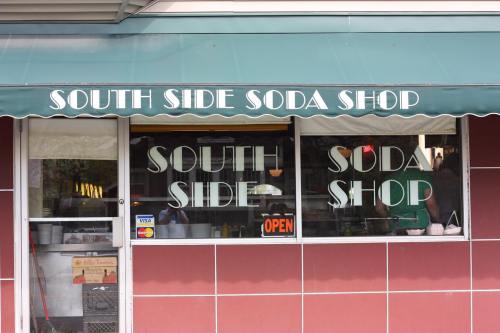 A storefront with a green awning reading "South Side Soda Shop" and an "Open" sign in the window.