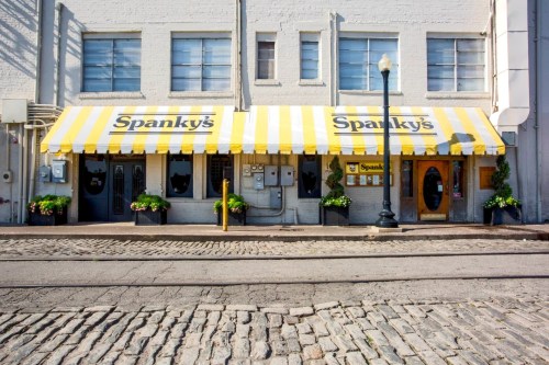 A restaurant with yellow and white striped awnings, named "Spanky's," located on a cobblestone street.