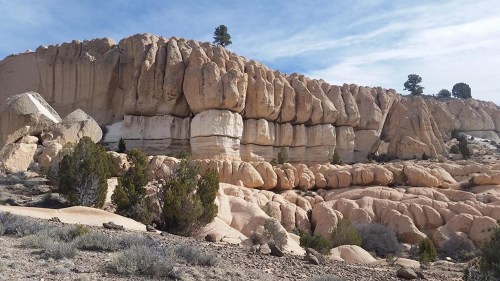 Rocky cliffside with layered formations and sparse vegetation under a blue sky.
