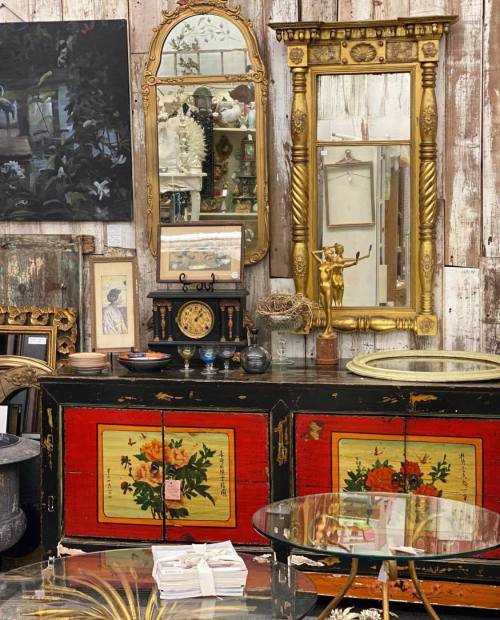 A vintage shop display featuring ornate mirrors, antique furniture, and decorative items against a rustic wooden backdrop.