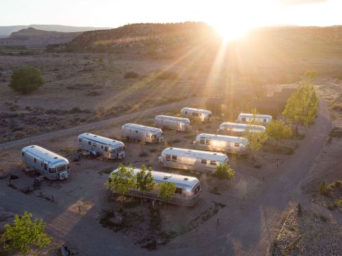 Aerial view of vintage Airstream trailers surrounded by desert landscape at sunset.