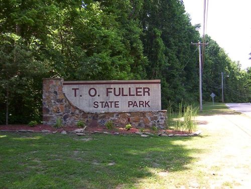 Sign for T.O. Fuller State Park, featuring stone structure and greenery, located near a road.