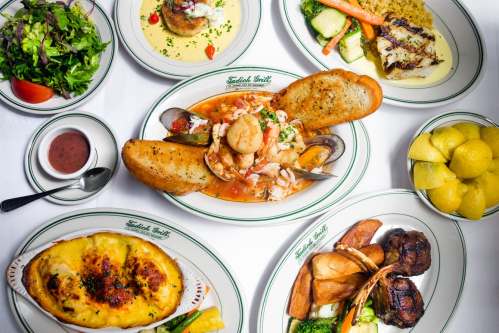 A spread of seafood dishes, including shrimp, grilled fish, and sides, with a fresh salad and lemon wedges.