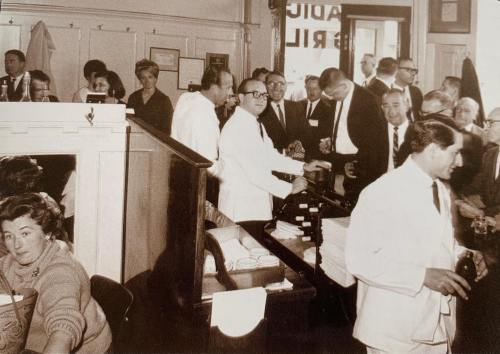 A busy vintage scene in a restaurant, featuring people in white coats and formal attire, socializing and dining.