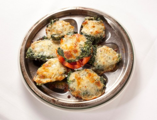 A silver platter with six baked spinach and cheese patties, garnished with a slice of tomato in the center.