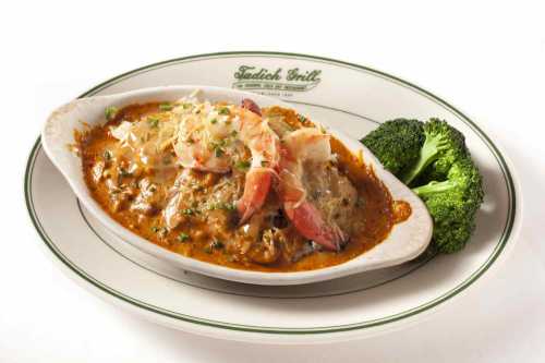 A creamy seafood dish with shrimp, served in a white dish alongside steamed broccoli on a plate.