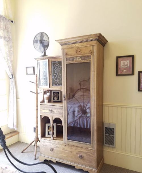 A cozy room featuring a wooden cabinet, a fan, and framed pictures on the wall, with soft lighting and a warm atmosphere.