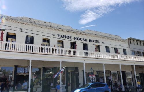 Historic Tahoe House Hotel with a white facade and balcony, set against a blue sky with scattered clouds.