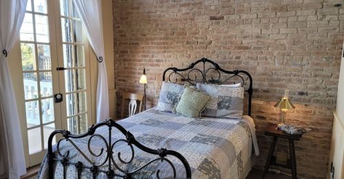 Cozy bedroom with a brick wall, a patterned quilt on a bed, and large windows letting in natural light.