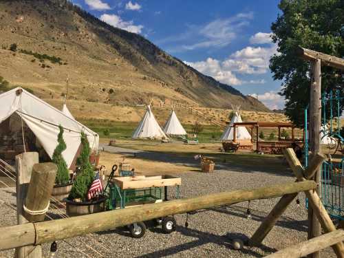 A scenic view of tipis and tents set against a mountainous landscape, with greenery and decorative elements in the foreground.