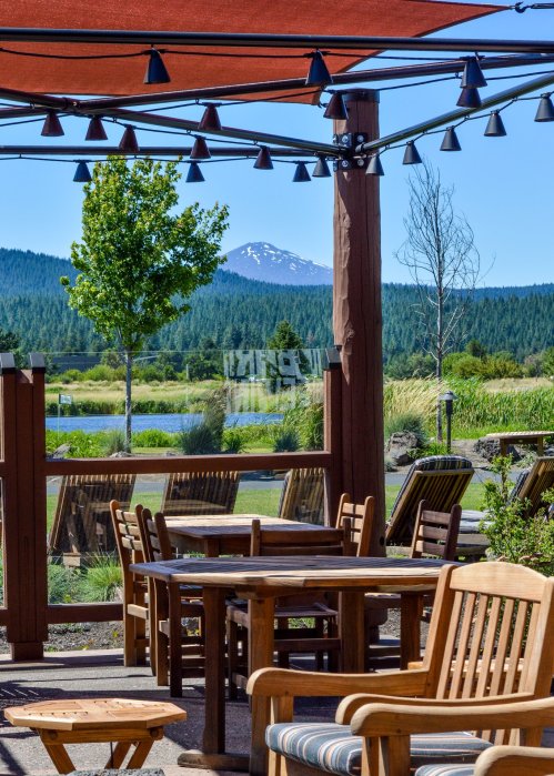 Outdoor seating area with wooden tables and chairs, overlooking a scenic view of mountains and greenery.