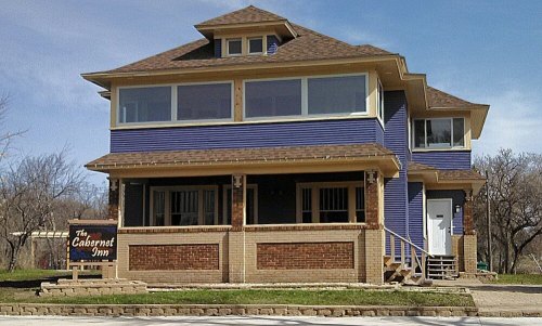 A large, two-story blue inn with a porch, featuring multiple windows and a sign that reads "The Cabernet Inn."