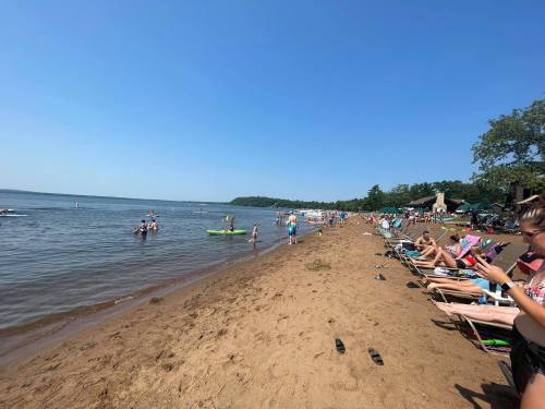 A busy beach scene with people sunbathing, swimming, and enjoying the water on a sunny day.