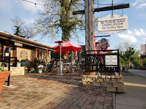A cozy outdoor dining area with red umbrellas, surrounded by greenery and a sign for "The Nashville House."
