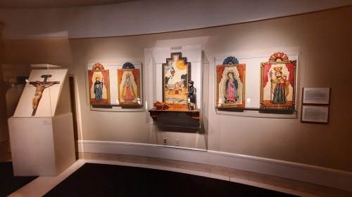A museum display featuring religious icons and a crucifix on the left, with colorful paintings on the right.