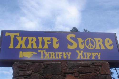 Sign for a thrift store named "Thrifty Hippy," featuring a peace symbol and a pointing hand.