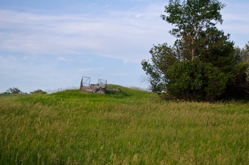 A grassy hill with a rusty metal structure and a tree in the background under a clear blue sky.