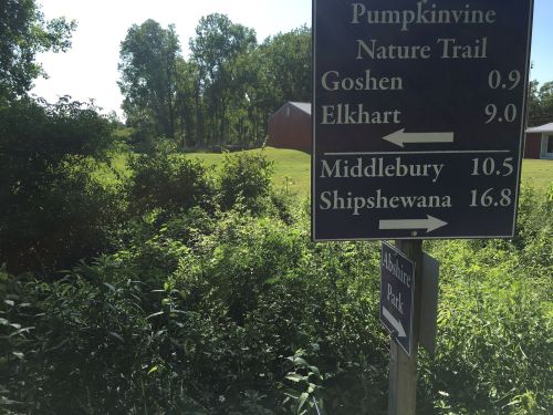 Signpost indicating directions and distances to various locations, including Pumpkinvine Nature Trail, Goshen, and Shipshewana.