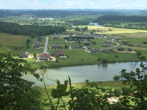 Aerial view of a scenic landscape featuring homes, a river, and green fields under a blue sky with clouds.
