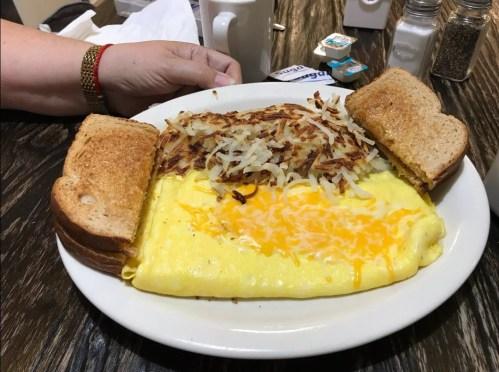 A plate with a cheese omelet, hash browns, and two slices of toasted bread, with a hand resting nearby.