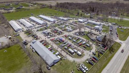Aerial view of a large outdoor event with tents, vehicles, and crowds in a rural setting.