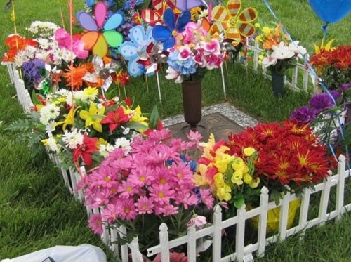 A colorful memorial garden surrounded by a white picket fence, filled with various flowers and decorative windmills.