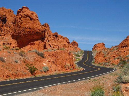 A winding road through vibrant red rock formations under a clear blue sky.