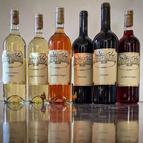 Six bottles of wine lined up on a counter, featuring various flavors: white cranberry, mango-citrus, strawberry, and more.