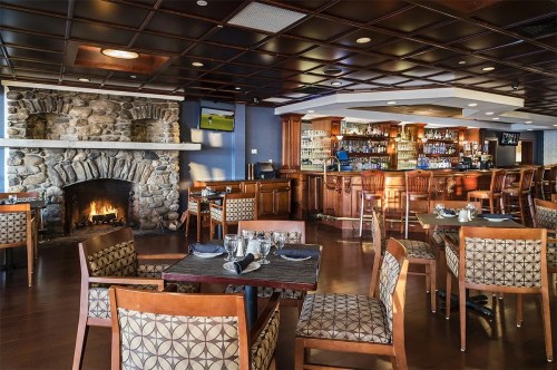 Cozy restaurant interior featuring a stone fireplace, bar area, and wooden tables with patterned chairs.