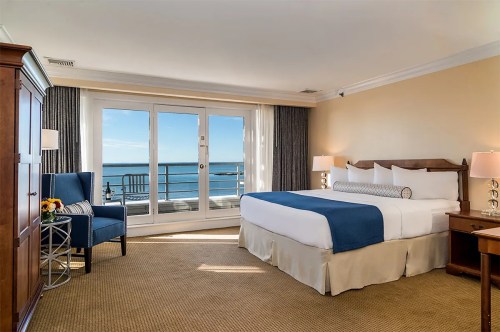Cozy hotel room with a king bed, ocean view, and balcony access, featuring warm lighting and elegant furnishings.