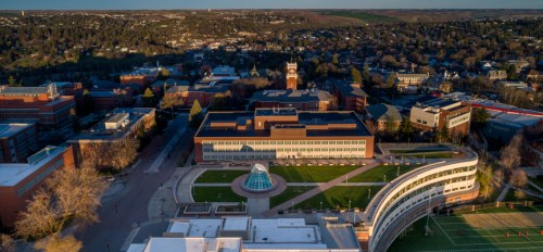 Aerial view of a university campus featuring buildings, a central plaza, and surrounding hills.