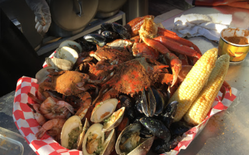 A large seafood platter with crabs, shrimp, mussels, clams, and corn, garnished with spices in a red-checkered basket.