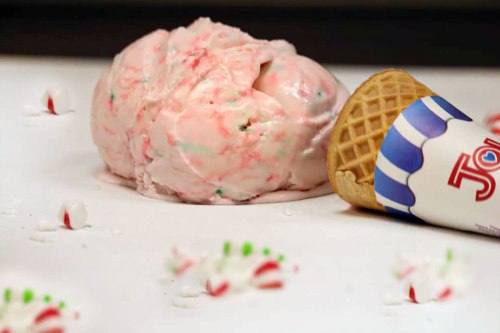 A scoop of pink peppermint ice cream next to a waffle cone, with scattered candy decorations on a white surface.