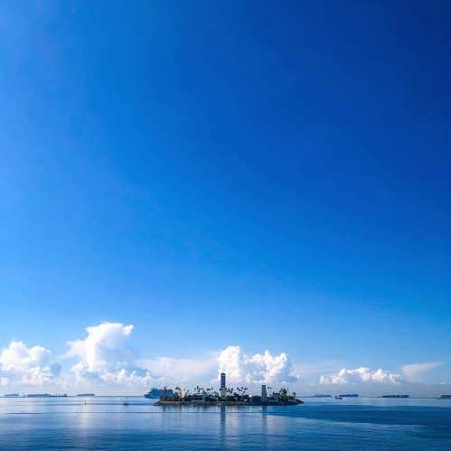 A serene view of an island surrounded by calm waters under a clear blue sky with fluffy white clouds.
