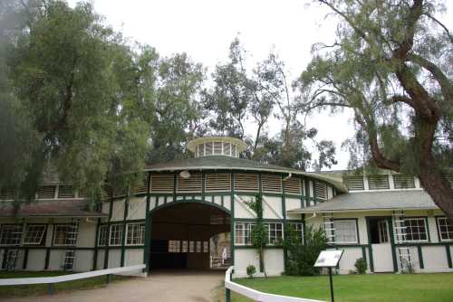 A round, green and white building surrounded by trees, featuring large windows and a central cupola.