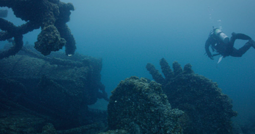 A diver explores a submerged shipwreck, surrounded by coral-covered structures and eerie underwater scenery.
