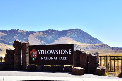 Sign for Yellowstone National Park with mountains in the background under a clear blue sky.