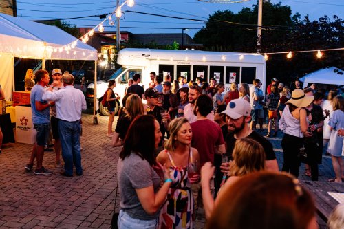 A lively outdoor event with people socializing, food trucks, and string lights illuminating the evening atmosphere.