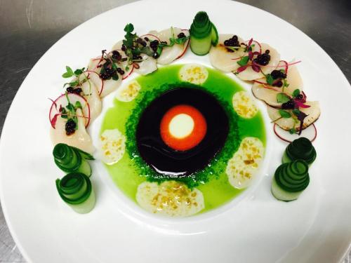 A beautifully plated dish featuring scallops, vibrant green sauce, and decorative vegetable garnishes in a circular design.
